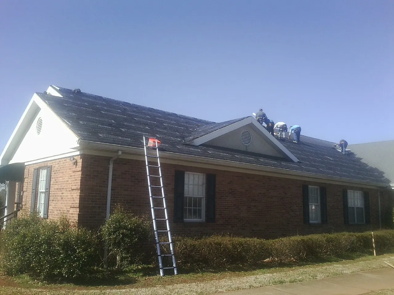 Crew tearing shingles off a brick ranch roof with a ladder set — Metal Roof Repair work by our crew in New Church