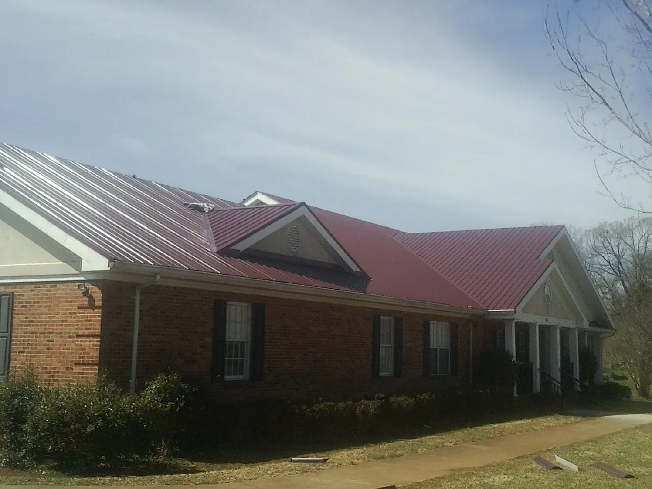 Red metal roof with gabled entries on a long brick building, from a Hail Damage Roof Repair job in New Church