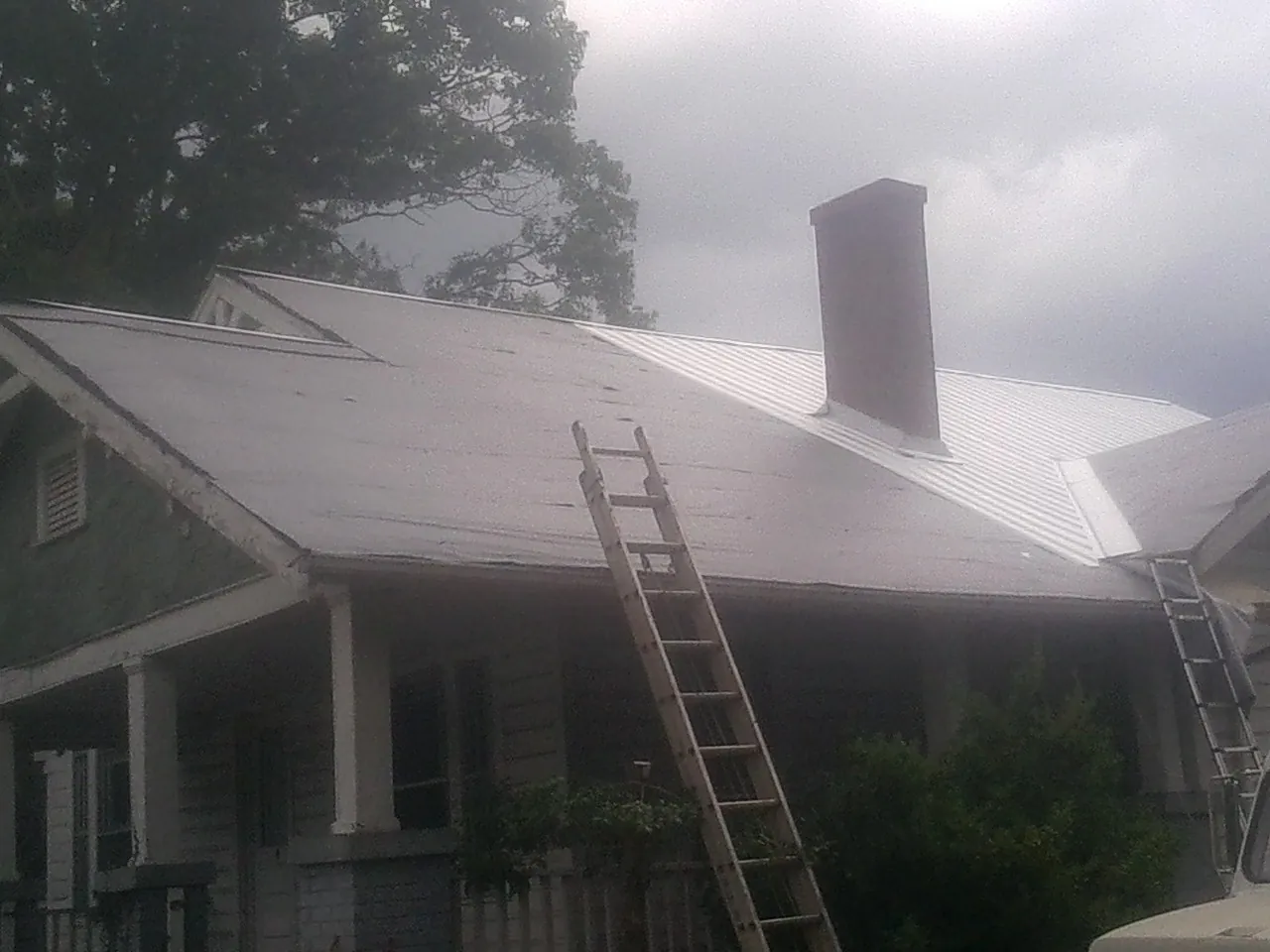 Ladders against a metal roof on an older home with a brick chimney in New Church