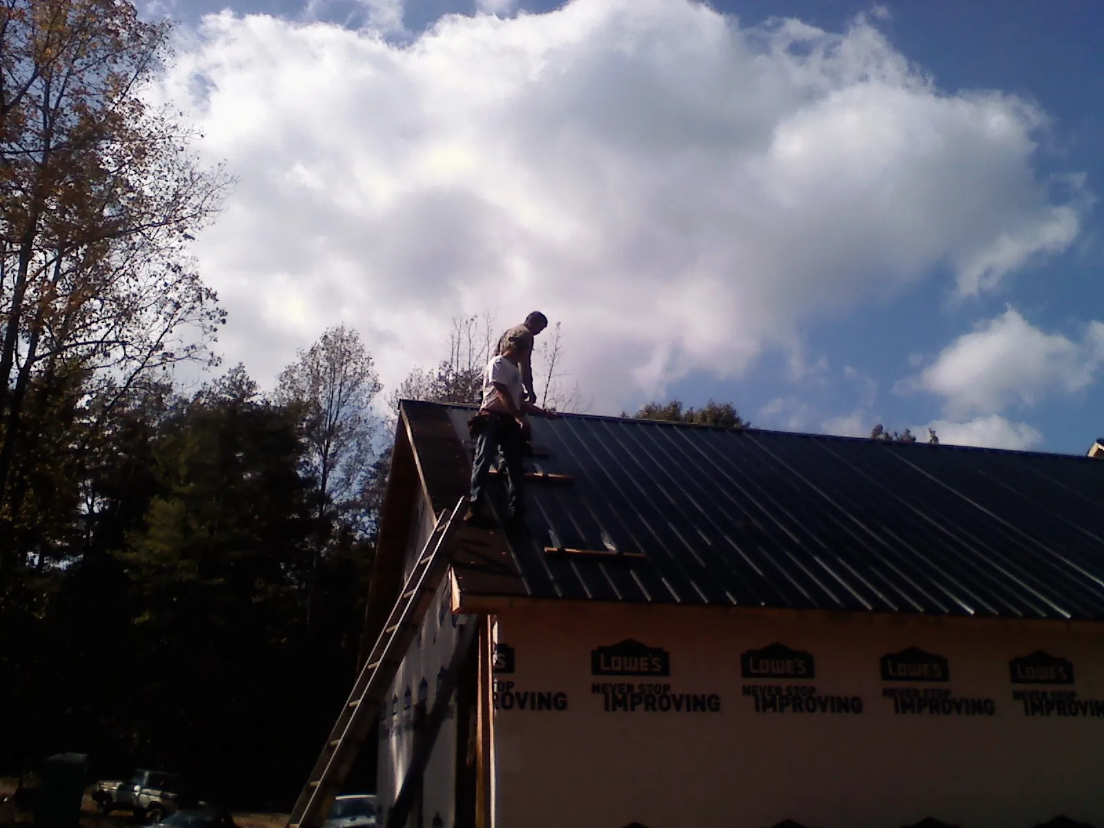 Roofer fastening dark metal panels high against a cloudy sky, from a Roof Inspection job in New Church