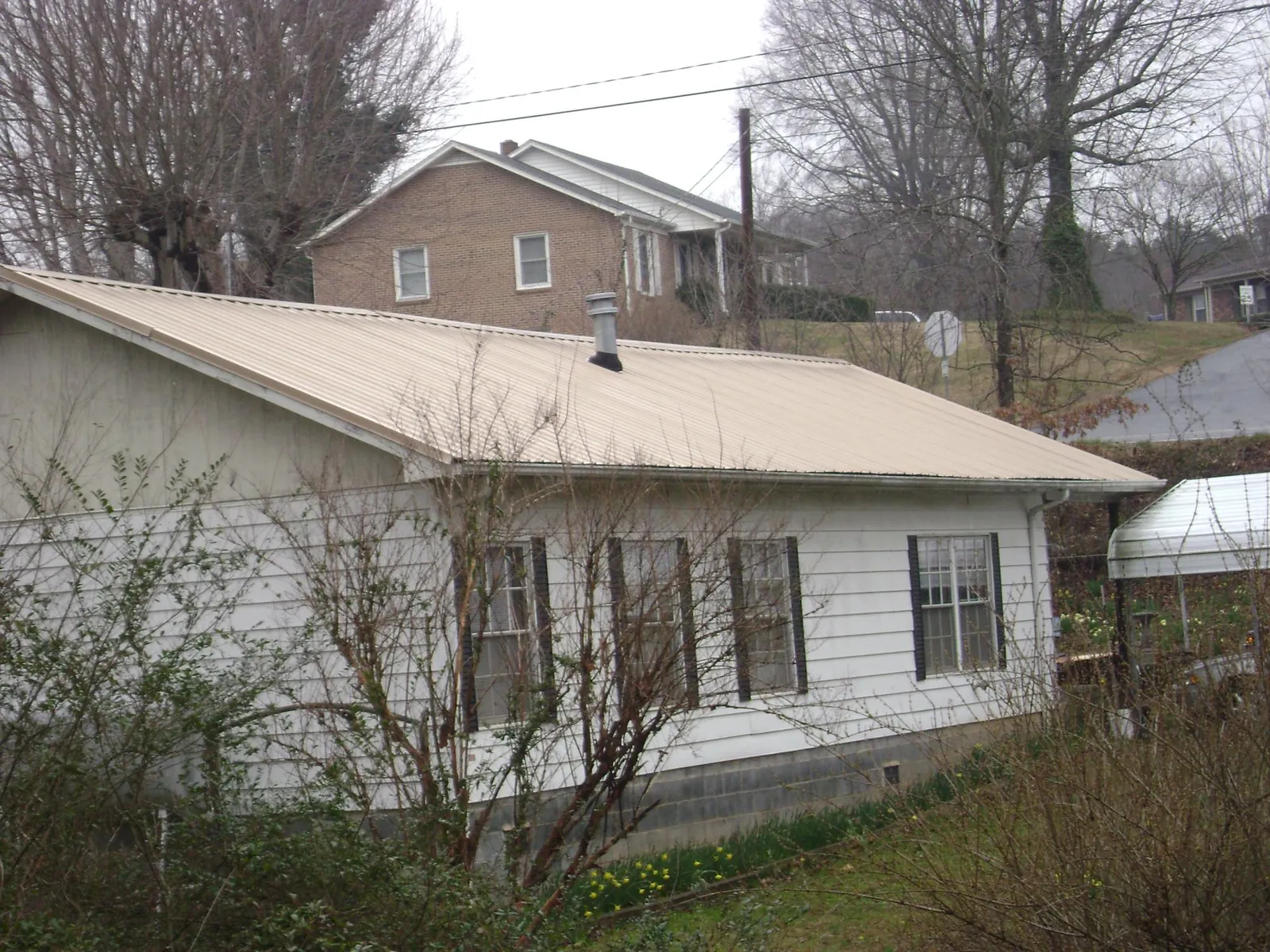 Tan metal roof on a white sided house set into a hillside — Commercial Roofing by Roofing Brothers in New Church
